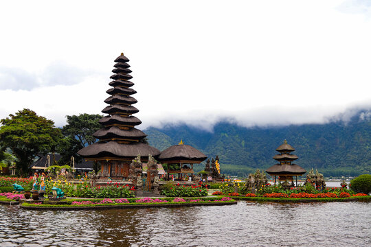 Iconic view of Pura Ulun Danu Beratan water temple on Lake Beratan, surrounded by colorful flower gardens and misty foggy mountains in Bedugul, Bali.