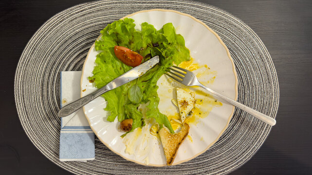 Empty dirty plate with food leftovers, knife and fork after finishing breakfast, top view
