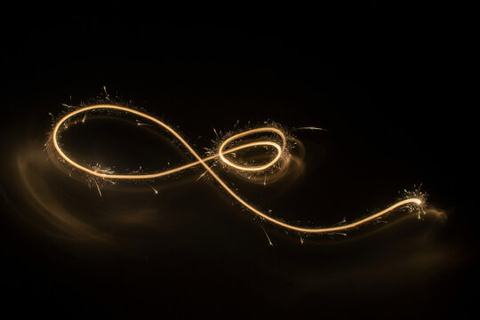 Golden light trail infinity symbol on black background, sparkling glowing swirl with starburst particles for luxury abstract design and celebration banner