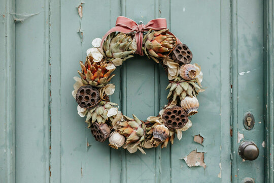 Rustic seashell and dried starfish wreath on weathered turquoise wooden door with metal handle, coastal home decor for summer entryway