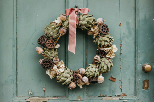 Rustic Christmas wreath with pink ribbon on weathered teal wooden door, natural dried flowers and pinecones, festive farmhouse holiday decor
