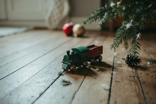 Rustic wooden floor with small green and red toy train, cozy Christmas still life with pine branches and ornaments for holiday background
