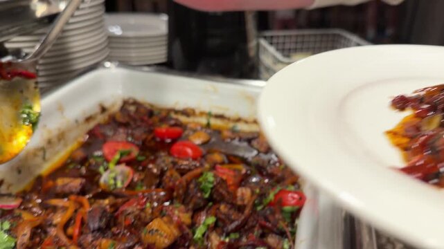A hand serving spicy stir-fried vegetables with tongs onto a clean white plate at a buffet station, capturing the essence of culinary catering service during an event or restaurant