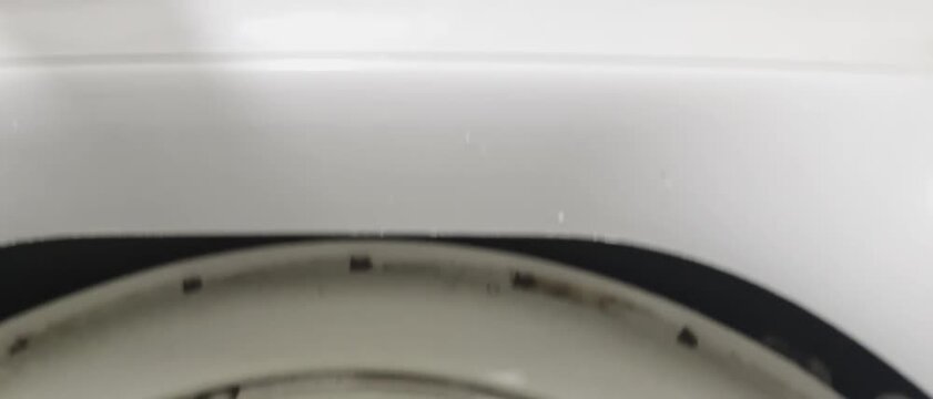 colorful domestic textiles, blue garments, and neon clothing items spinning inside a washing machine drum under splashing water. Target use cases include home appliance advertising, laundry detergent 