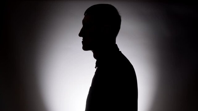 Front view silhouette of an anonymous man in shirt against dramatic backlight background. Mysterious profile concept for privacy, incognito, crime, or psychological topics.