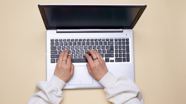 Top view of woman typing on laptop keyboard with hands visible. Flat lay shot showcasing computer display and female workspace from overhead perspective.