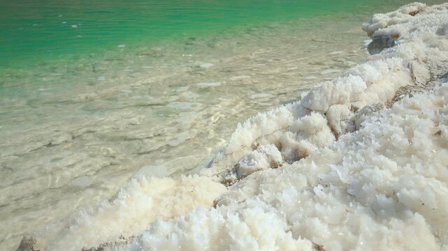 White crystalline salt formations at shore of Dead Sea on Jordan side, calm clear water near, closeup detail