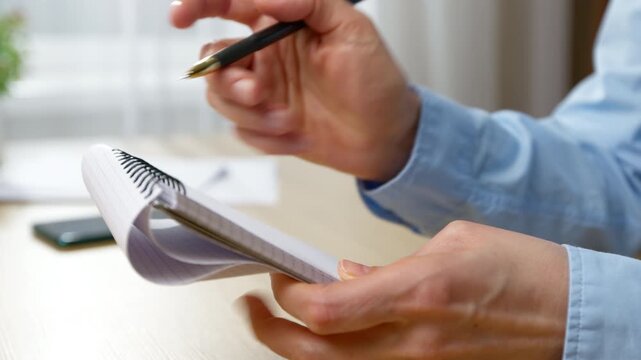 Person writing notes in spiral paper pad with pen. Hand taking information during business planning process.