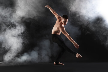 Professional dancer practicing moves on black background with smoke © New Africa