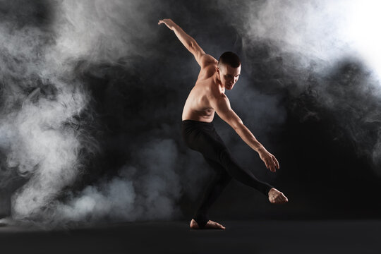 Professional dancer practicing moves on black background with smoke