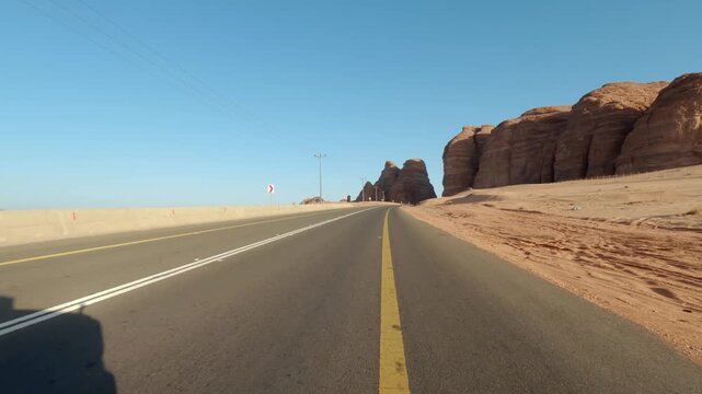 Driving on main road in Al Ula desert at Saudi Arabia, car passes near tall rocky formations