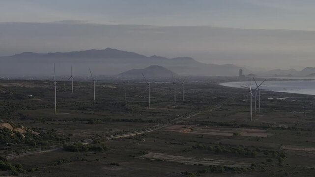 Aerial drone footage of Wind Farm in Phuoc Dinh, Khanh Hoa, Vietnam, featuring giant wind turbines along the coastal landscape, showcasing renewable energy, sustainable power and clean technology.