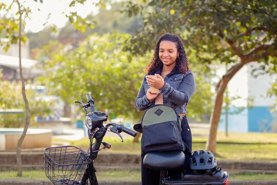 Young Black Brazilian woman using her smartphone beside an electric bicycle, representing urban mobility, connected commuting, and sustainable transportation.