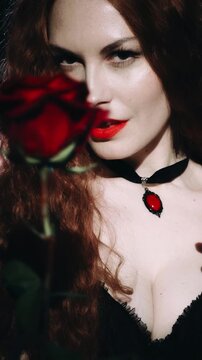 vampire woman licks drops of blood fingers hands, red lips evil beauty face sexy girl white teeth fangs. hand holding red rose giving flower. halloween holiday make-up, invites to go at gothic party.