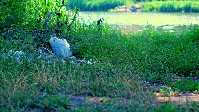 Multiple plastic bottles and trash items lying on green grass near river shore highlighting plastic waste contamination