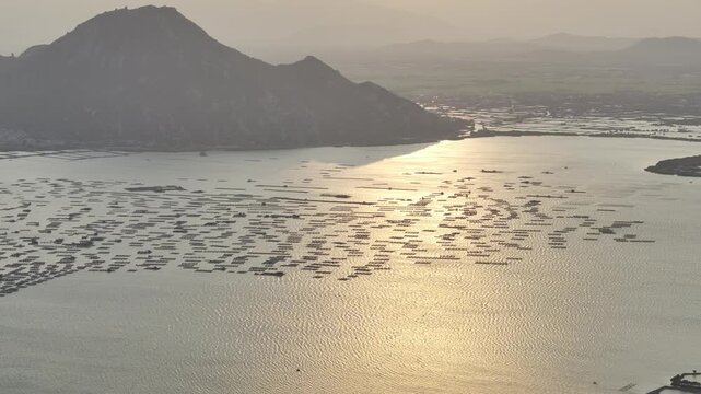 Aerial drone footage of sunset over Dam Nai Lagoon, Khanh Hoa, Vietnam, featuring golden reflections, tranquil waters, fishing boats and breathtaking coastal landscape at golden hour.