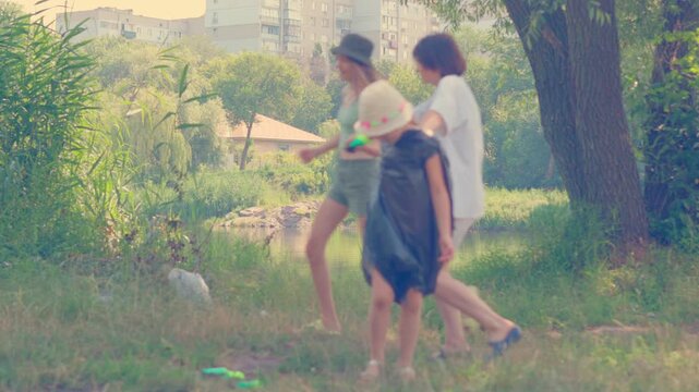 Kids carrying black air mattress across green field near river on bright summer day during family outing