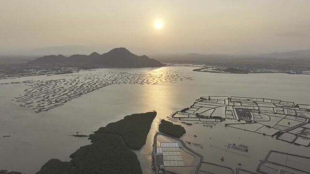 Aerial drone footage of sunset over Dam Nai Lagoon, Khanh Hoa, Vietnam, featuring golden reflections, tranquil waters, fishing boats and breathtaking coastal landscape at golden hour.
