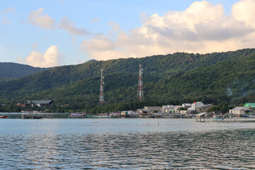Fototapeta premium Beautiful view of a coastal fishing village nestled along calm ocean waters with lush green tropical mountains and cloudy skies in Karimunjawa, Jepara, Central Java, Indonesia during late afternoon.