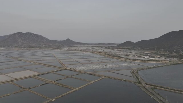 Aerial drone footage of Phuong Cuu Salt Fields in Khanh Hoa, Vietnam, showcasing traditional sea salt production, geometric salt ponds, coastal landscape and sustainable local industry.