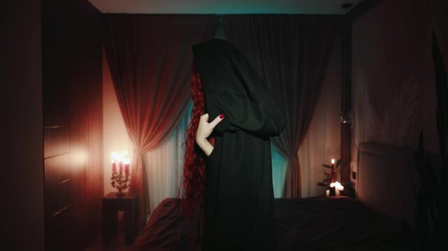 Happy beauty gothic woman takes off cloak cape hood waving beckoning hand gesture invitation to follow me. Dark night room. Fantasy girl evil evening makeup lips long red hair, black dress old style