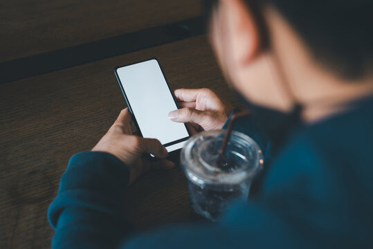 Person using mobile phone with empty mockup screen and iced coffee on wooden table, authentic photo, not AI.