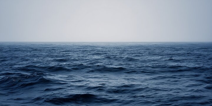 Calm deep blue ocean water surface under foggy mist sky background with soft calm waves on horizon, minimal seascape