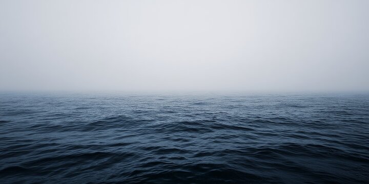 Vast open deep blue ocean water waves surface beneath overcast misty sky at calm sea horizon, minimal seascape