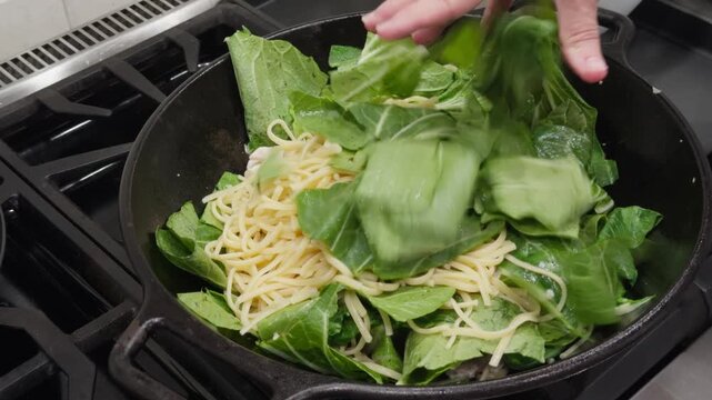 Stir frying chicken, bok choy, and noodles in a wok