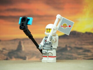 Naklejka premium Indonesia - June 17, 2025 : Mini toy of action figure at table with blurred background. Miniature diorama photography concept design. Astronaut character take a photo with alien at space. Selfie stick