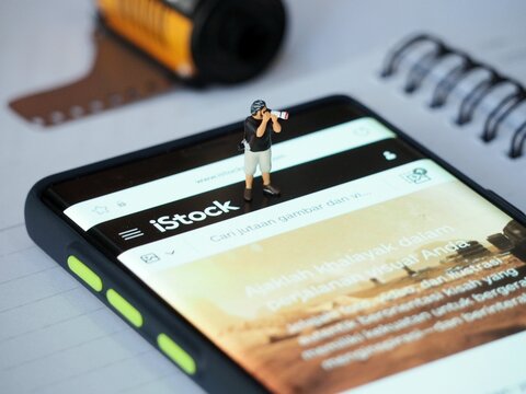 Indonesia - May 12, 2023 : View of smartphone with Istock mobile app on screen display at table with mini toy figure. Background is blurred. Social media photography concept design