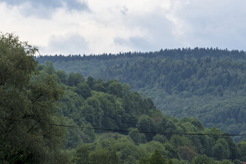 Beskidy w malowniczy, pochmurny, wiosenny dzień. Łagodne zbocza Beskidów w soczyście zielonej, pochmurnej, wiosennej scenerii. Krajobraz porastają gęste lasy, w których są drzewa liściaste i iglaste © Grzegorz