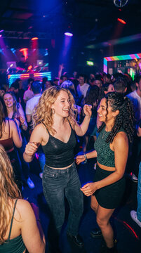 Dos amigas disfrutan de una noche de fiesta en una discoteca, bailando y sonriendo bajo luces de ne&oacute;n, capturando la energ&iacute;a, diversi&oacute;n y ambiente de la vida nocturna.