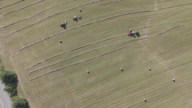 Aerial drone view of tractor working farmland with rows of hay bales