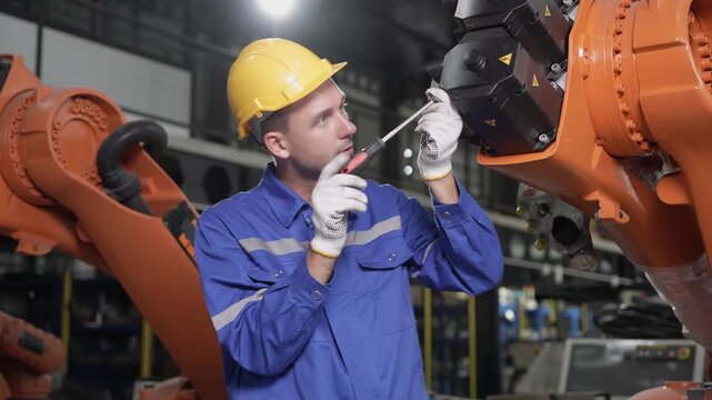 Technician repairing robotic arm in smart factory, Industrial engineer maintaining automated machine in plant, Worker fixing industrial robot arm with screwdriver