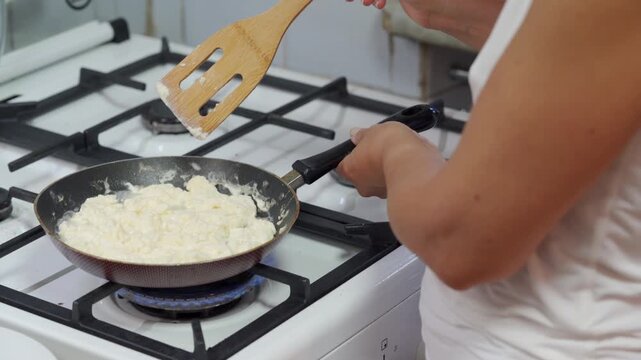 A focused cook prepares fluffy scrambled eggs in a hot pan on a gas stove. Making this warm breakfast brings a cozy, comforting feeling to the peaceful kitchen.
