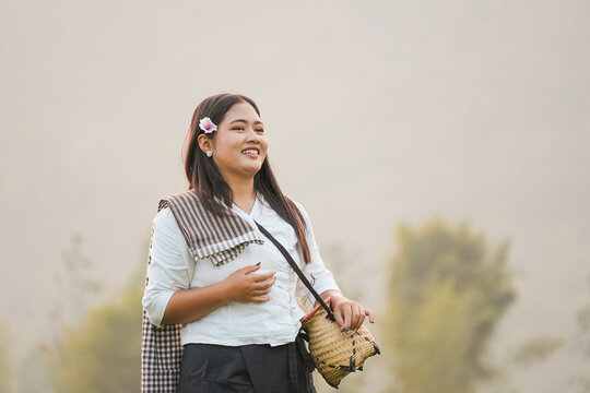 A beautiful smiling Asian woman in traditional local clothing holding a woven basket in a rural field during sunset, authentic portrait of local lifestyle and simple happiness.