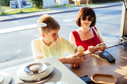 Mature mother and teenage son ordering ice cream at street kiosk on sunny summer evening