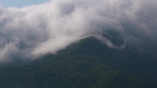 White clouds flowing over green mountain peak