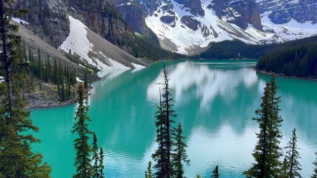 Beautiful view on the Moraine Lake in National Park of Banff, Canada. Stunning view of a turquoise mountain lake surrounded by evergreen trees and snow-capped peaks.
