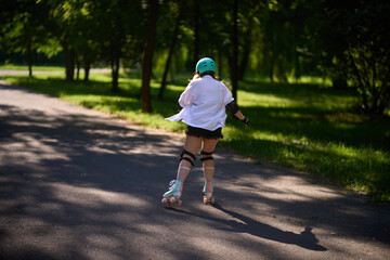 Fototapeta premium Girl skating on a path in a park on a sunny day with trees around her