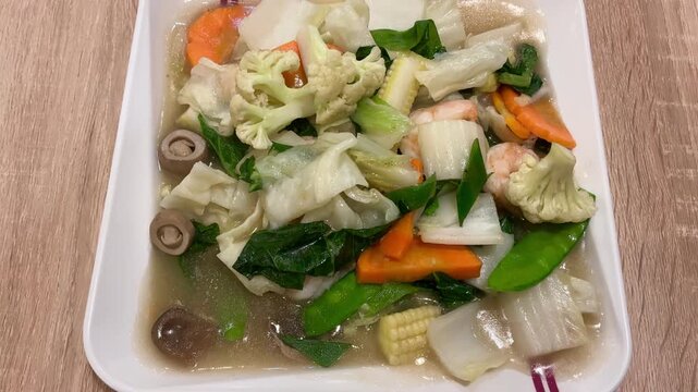 Overhead video of a healthy stir fried mixed vegetables dish with shrimp. The colorful dish features cabbage, carrots, cauliflower, baby corn and snow peas in a savory sauce served on a white plate.