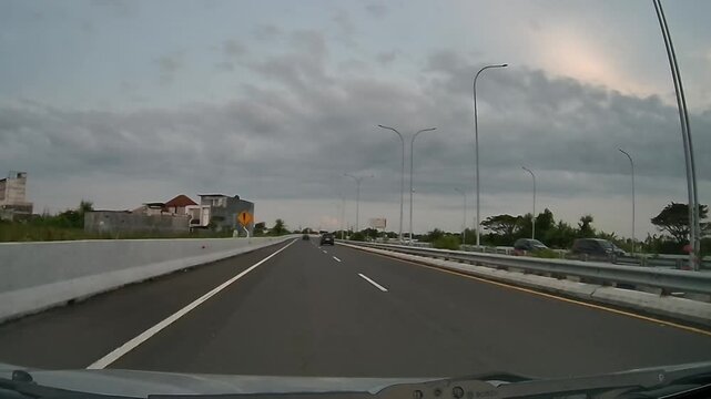 Front Dashcam Driving on Waru&ndash;Juanda Toll Road Passing Blue Pedestrian Bridge Under Cloudy Afternoon Sky, East Java, Indonesia