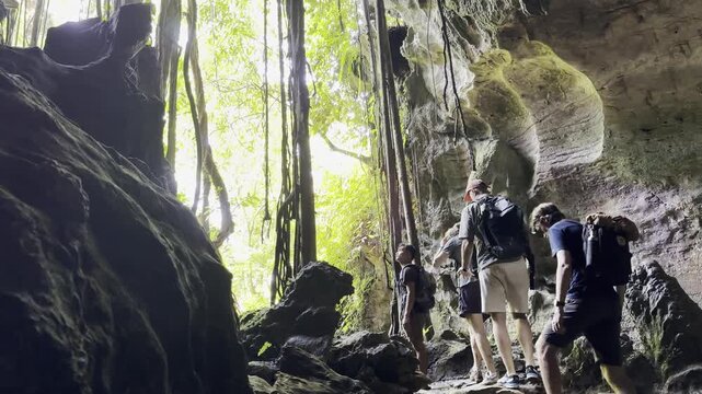 Small group of tourists walks through two chambers of Bukit Lawang Bat Cave, exploring the limestone cave beneath a colony of bats. North Sumatra, Indonesia.