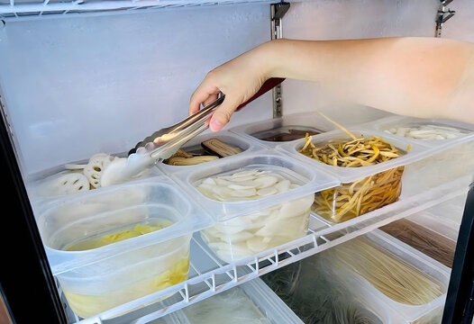 Person Using Metal Tongs to Pick Sliced Lotus Root from Plastic Container in Refrigerator