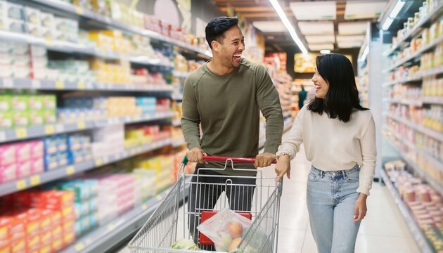 Couple shopping together in a grocery store while pushing a cart filled with fruits and vegetables