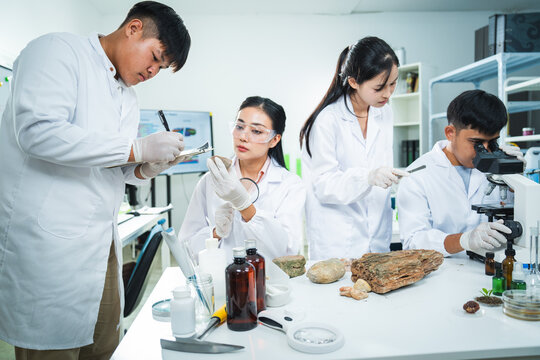 Scientist laboratory microscope research experiment sample protective eyewear lab coat team examines natural specimen with focused expression during biology study in modern workspace