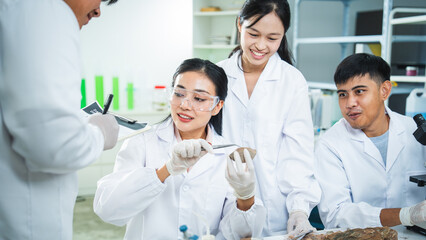 Fototapeta premium Scientist laboratory research team student microscope, Asian young adult group in lab coat and protective eyewear conduct experiment with pipette, tablet, glassware, smiling teamwork