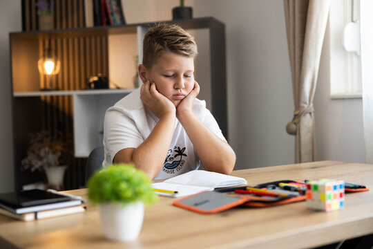 Boy resting his head on hands, showing boredom or frustration while studying at a desk inside his room
