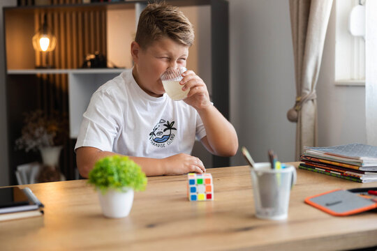 Young boy making a funny face, puckering due to the sour taste while drinking citrus juice from a glass at his home desk